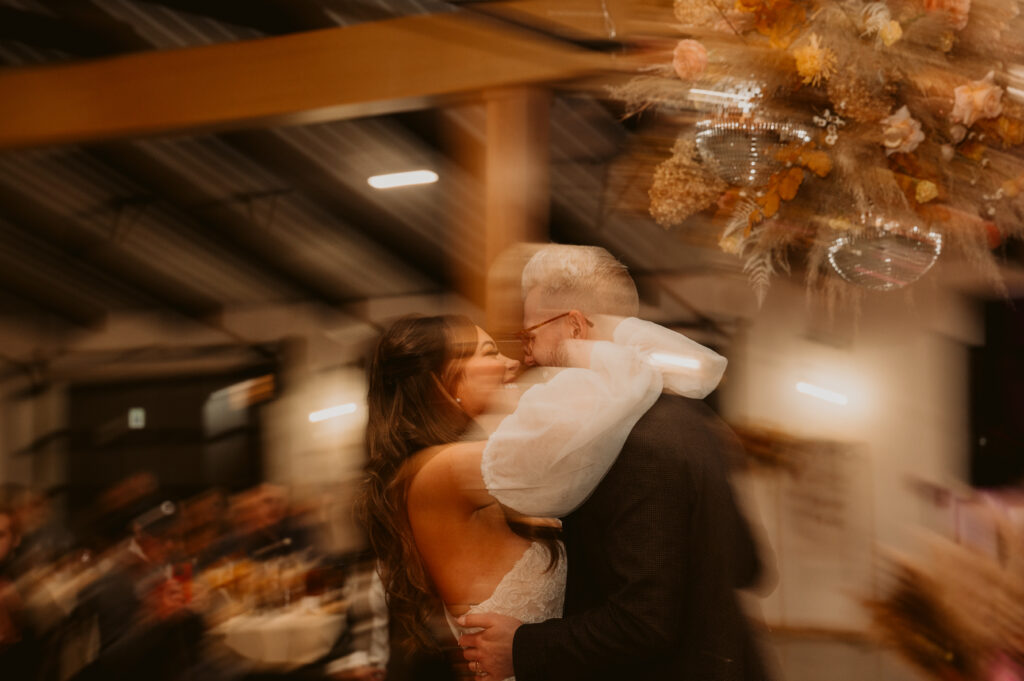 A bride and groom kissing above a terracotta, golden mustard, toffee, pampas disco ball flower installation at Meadville wedding venue The Harper.